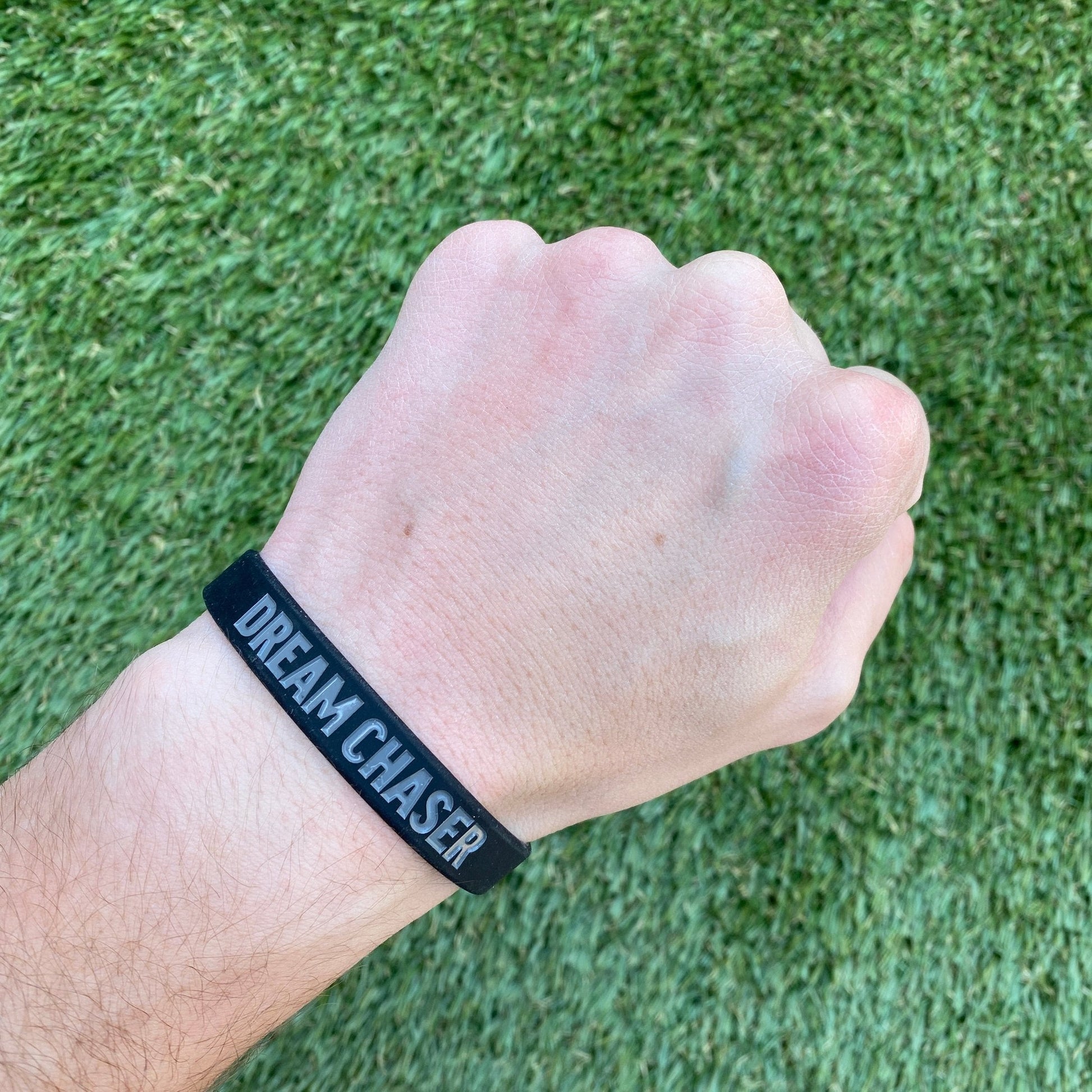 Hand wearing a black wristband with 'DREAM CHASER' text on green grass background