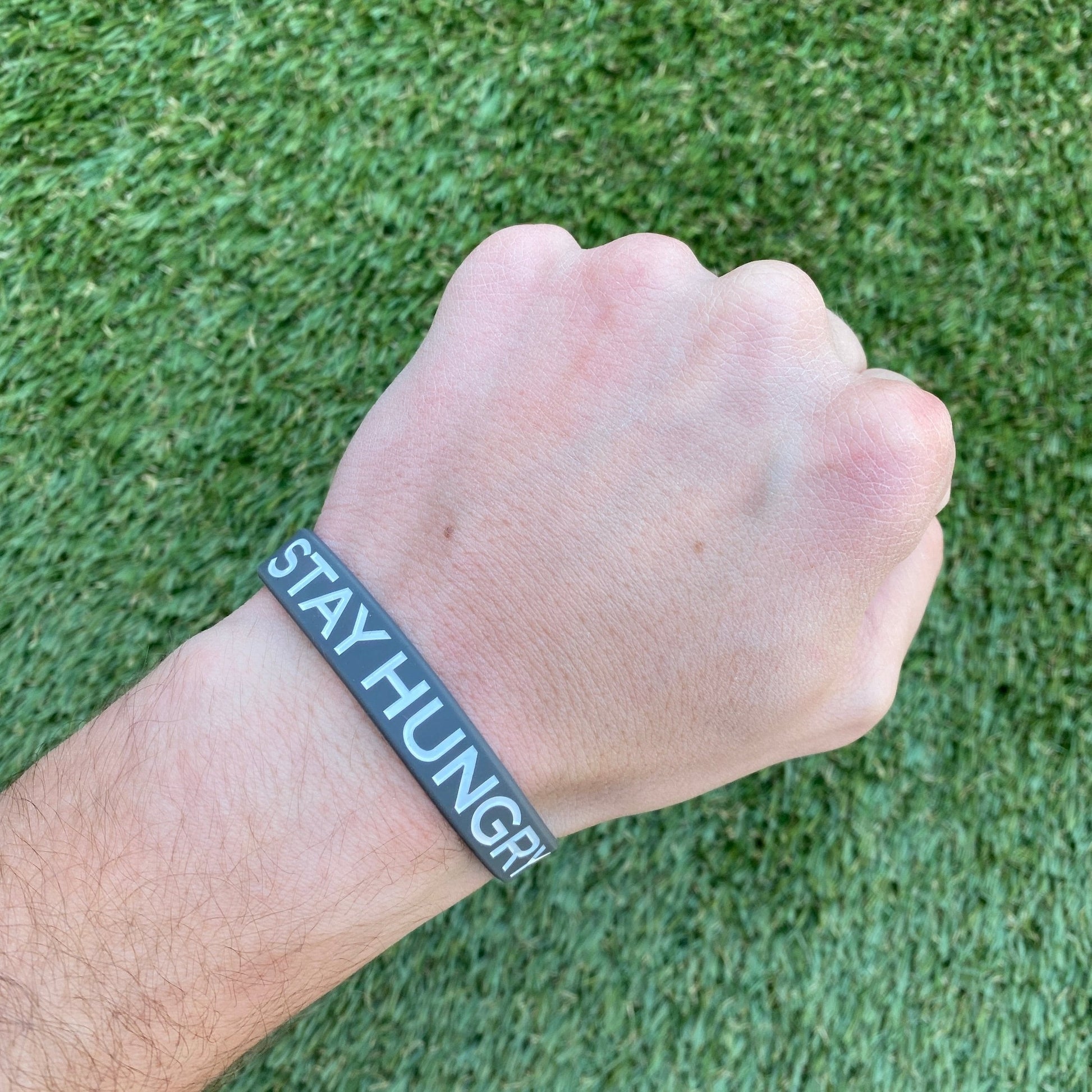 Hand wearing a wristband with 'STAY HUNGRY' text on a grass background