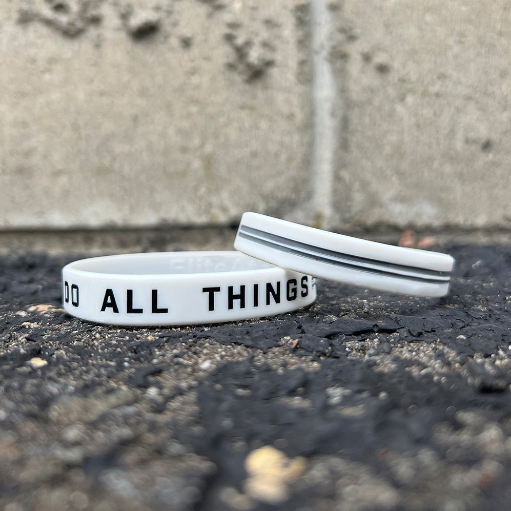 Collection of Two white wristbands with text on a concrete surface in a gallery layout