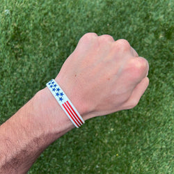 Collection of Hand wearing a wristband with an American flag design on a grass background in a gallery layout
