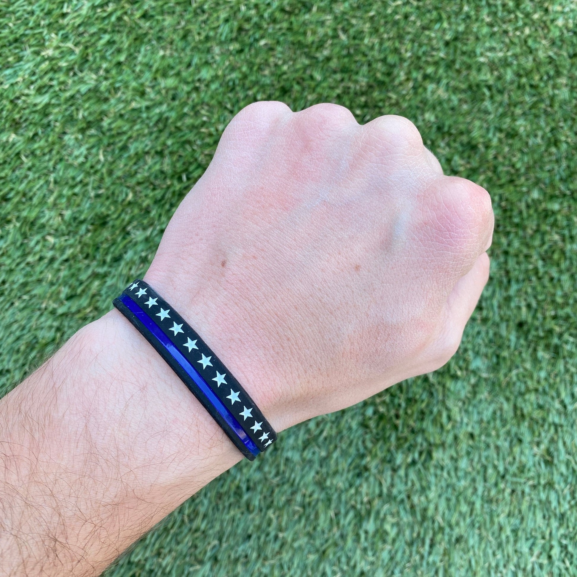Hand wearing a blue and black bracelet with star pattern on grass background