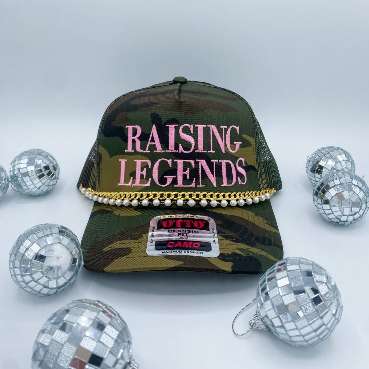 Camouflage cap with 'Raising Legends' text, surrounded by disco balls on a light gray background